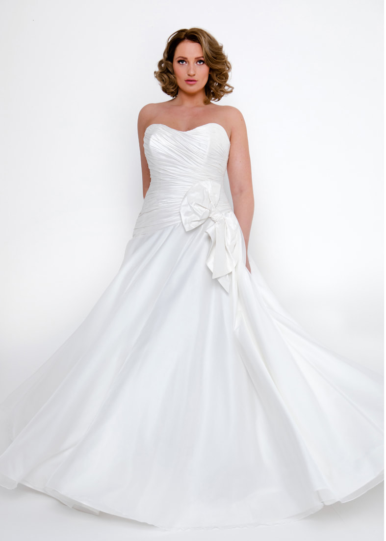 Strapless wedding dres with a full skirt and pleated bodice. Adorned with a large bow detail
