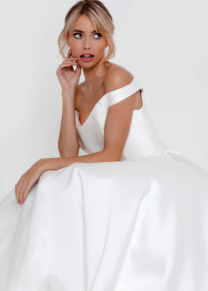 Seated bride wearing a ballgown wedding dress with an off the shoulder neckline