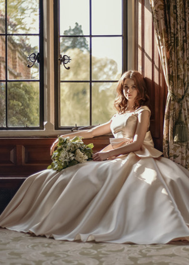Seated shot of the Caring wedding dress with a full skirt. Worn with the Luna oversize bow belt