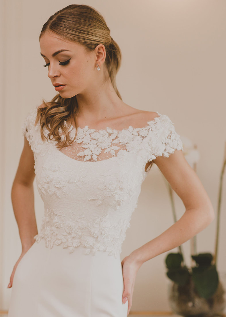 Lace cropped back fastening bridal shrug with cap sleeves and lace embellished neckline. Shown worn with a strapless bodice and full bridal skirt with thigh split 