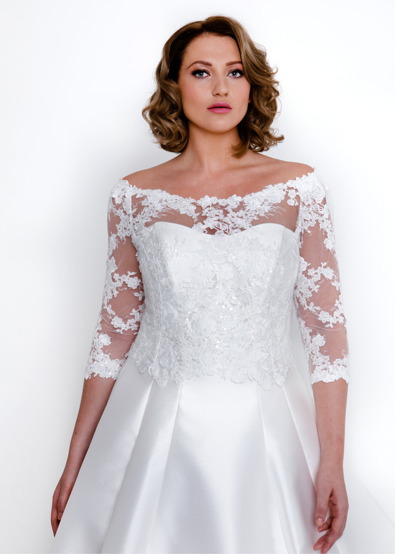 Off the shoulder embroidered tulle bridal shrug with back fastening. Shown worn over a strapless wedding dress