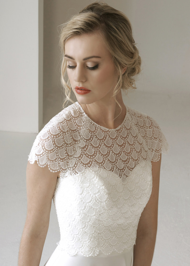 modern style back fastening bridal shrug with capsleeves and a high neck. Made from embroidered lace with an art deco fan pattern and embellised with seed pearls