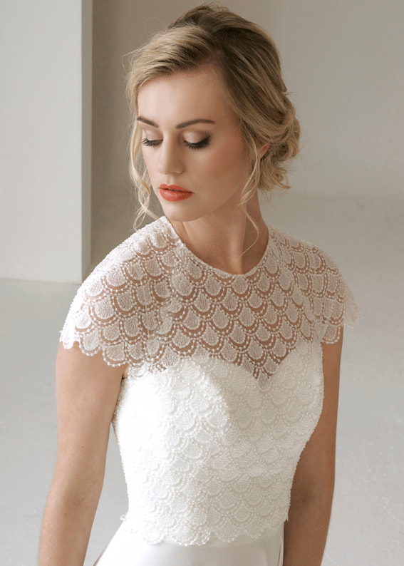 Ornate lace bridal shrug embellished with tiny seed pearls. Shown worn over a strapless wedding dress